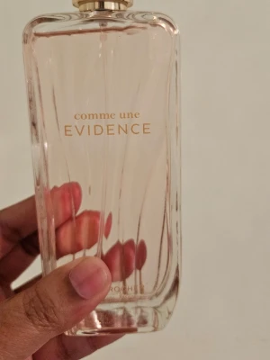 Comme une Evidence Eau de Parfum - Comme une Evidence Eau de Parfum från Yves Rocher kommer i en elegant, rektangulär glasflaska med ljusrosa toner och gulddetaljer. Flaskan rymmer 100 ml och har en stilren design med subtila linjer och guldtext. Doften är feminin och klassisk. Har ej använt, bara doftat . Bruten förpackning. Kan mötas upp i stan  (T-Centralen,  Stockholm)