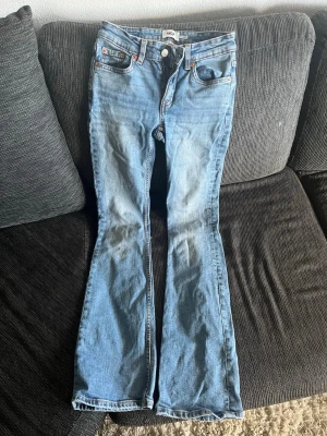 Ljusblå bootcut jeans - Säljer ett par ljusblå bootcut jeans med klassisk femficksdesign och orangea sömmar. Jeansen har normal midja och är tillverkade i denim med lätt tvättad look. Perfekta för dig som gillar retrostil och bekväma passformer.