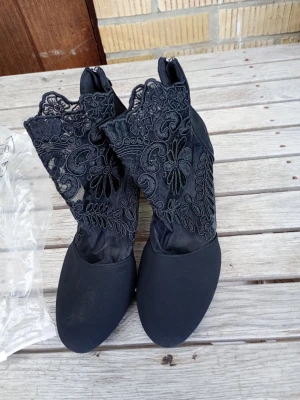 Svarta spetsstövletter med blommönster - Unika svarta stövletter med rund tå och hög skaft i spets med blommigt mönster. Skorna har en elegant och feminin look med transparenta detaljer i skaftet. Materialet är en mix av tyg och spets som ger en cool kontrast.