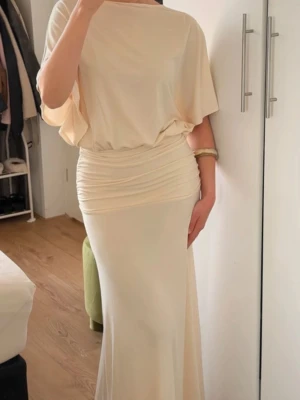 Ljusbeige långklänning med drapering - Säljer en elegant ljusbeige långklänning med lös passform upptill och draperad midja. Storlek S. Endast testad.