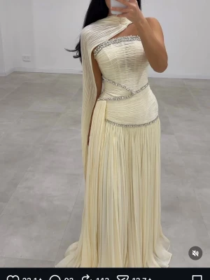Festklänning från Laselins  - Elegant gul långklänning från Laselins Dresses från Nederländerna köpt för 3500kr, med plisserad design och glittriga detaljer längs kanterna. Klänningen  är ärmlös och tillkommer med ett svepande tyg över  axelarna. 