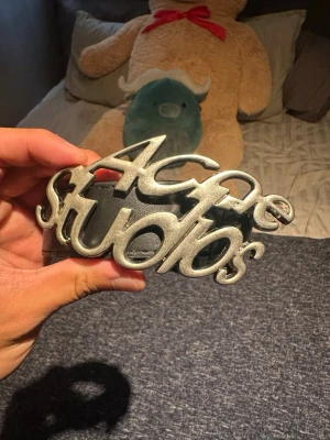 Acne Studios svart bälte med silverdetalj - Snyggt svart bälte från Acne Studios med en stor, iögonfallande silverspänne där loggan står i skrivstil. Bältet är gjort i skinn och passar perfekt för att lyfta vilken outfit som helst.