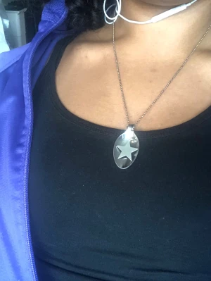 Silverfärgat halsband med stjärnhänge - Snyggt halsband i silverfärg med ett ovalt sked hänge med en stjärna i mitten. Kedjan är tunn och metallisk, och hänget har en modern, stilren design. Perfekt för dig som gillar unika detaljer och vill sticka ut lite extra.
