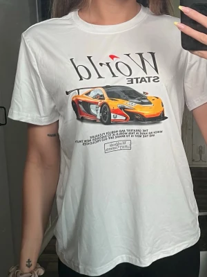 Vit t-shirt med sportbilsmotiv - Vit t-shirt med tryck av en gul sportbil och texten 'World State' på bröstet. T-shirten har rund hals och korta ärmar, perfekt för dig som gillar bilar och streetstyle. Skön passform och lätt material som känns bekvämt hela dagen.