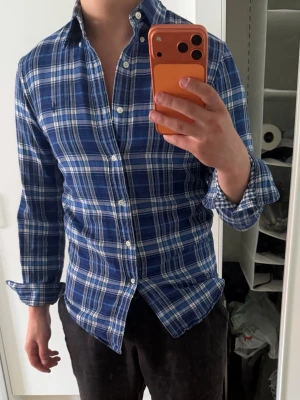 Ralph lauren skjorta - Säljer en blå rutig skjorta från Ralph Lauren med vita och ljusblå rutor. Skjortan har klassisk krage, långa ärmar och knäppning framtill. Perfekt för en avslappnad men ändå stilren look.