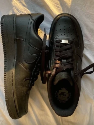 Svarta Nike Air Force 1 sneakers - Klassiska helsvarta Nike Air Force 1 sneakers i läder med svart sula och svarta skosnören. Storlek 37.5. Skorna är använda men i gott skick. 
