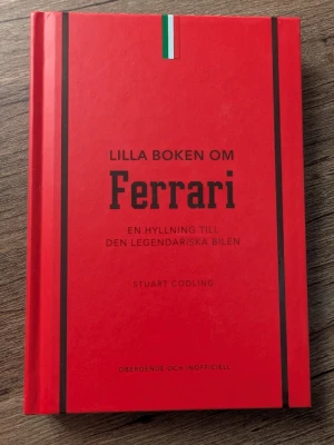 Lilla boken om Ferrari - En snyggt designad röd bok med svarta detaljer och italiensk flagga på omslaget. Boken är skriven av Stuart Codling och handlar om Ferrari, med fokus på hyllning till den legendariska bilen. Perfekt för bilentusiaster och Ferrari-fans.