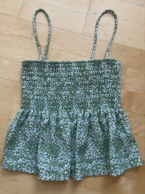Grön blommig linnetopp med smock - Söt grön linnetopp med vita små blommor och smockad överdel, från Gina i strl XS. Toppen har tunna axelband och en luftig, lätt utsvängd passform. Har även en liknande topp som jag säljer, paketpris kan ordnas isf🌸