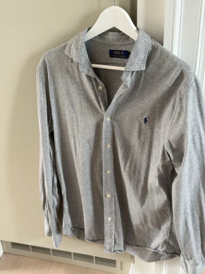 Ralph Lauren Jersey Shirt  - Snygg grå skjorta från Polo Ralph Lauren med klassisk krage och knäppning framtill. Skjortan har lång ärm och den ikoniska broderade loggan på bröstet. Knappt använd, mycket gott skick. Priset kan diskuteras vid snabb och seriös affär! 