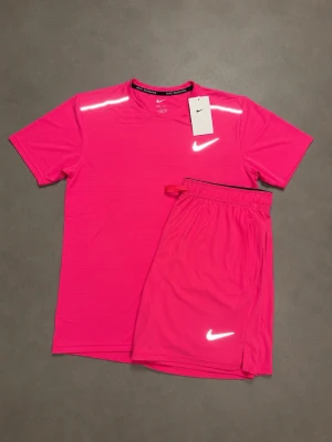 Nike Miller set - Säljer ett sportigt träningsset från Nike i rosa. Setet består av en kortärmad t-shirt och matchande shorts, båda med Nike-logga och reflexdetaljer. Perfekt för gymmet eller löprundan. Materialet är lätt och andas, vilket gör det bekvämt under träning. STORLEKSINFO: Lappen säger L (Kina), men motsvarar en EU Small (S). • Bröst: 95–101 cm. • Midja: 88–94 cm.
