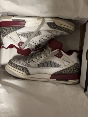 Vita och vinröda sneakers med mönster - Snygga sneakers i vitt och vinrött med gråa detaljer och klassiskt elefantmönster på tå och häl. Skorna har meshpaneler på sidorna och tjock sula för extra komfort. Perfekta för dig som gillar streetwear och vill sticka ut. Men de är lite skadade där inne i baksidan.