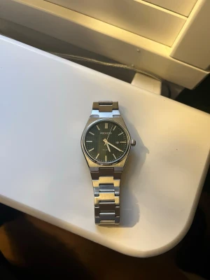  silverfärgad klocka - Stilren klocka med silverfärgad länk i metall och mörk urtavla. Klassisk design med tydliga markeringar och datumvisning. Perfekt för dig som gillar en enkel men snygg look.