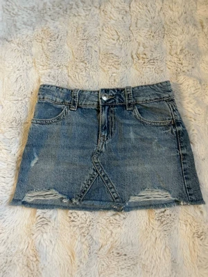 Blå jeanskjol med slitningar - Snygg blå jeanskjol i kort modell med slitna detaljer framtill. Jag säljer den för den inte passar längre. De står 146 i storlek men passar på xxs