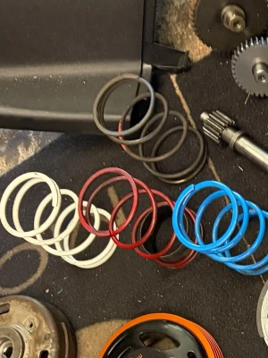 Fjädrar och variatorvikter till moped - Säljer ett gäng färgglada fjädrar i svart, vitt, rött och blått samt variatorvikter i en röd plastask. Perfekt för dig som vill trimma eller justera din moped. Passar till olika modeller och är tillverkade i metall och plast.