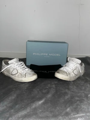 Vita Philippe Model sneakers - Säljer ett par vita Philippe Model sneakers med klassisk låg silhuett. Skorna har vita skosnören, svarta yttersulor och detaljer i läder. Perfekta för dig som gillar stilrena och tidlösa sneakers. Vid frågor hör av dig och priset kan alltid diskuteras 