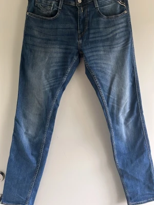 Blå jeans från Replay (Anbass) - Säljer ett par klassiska blå jeans från Replay. Jeansen har snygga slitningar och kontrastsömmar, samt en patch med logga bak i midjan. Tillverkade i slitstark denim som passar perfekt till en avslappnad stil.