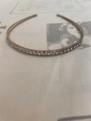Tunt diadem med strassdetaljer - Snyggt och smalt diadem i metall med glittrande strass längs hela ovansidan. Perfekt för att ge en extra touch till din look. Diademet har en elegant och minimalistisk design i silverfärg.