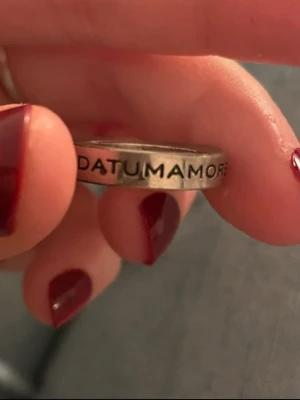 Datum amore defendemdum Marc Jacobs  - Säljer en stilren silverfärgad ring i metall med ingraverad latinsk text runt hela ringen. Ringen har en klassisk, slät form och texten ger den en unik och personlig touch. Perfekt för dig som gillar accessoarer med betydelsefulla detaljer.