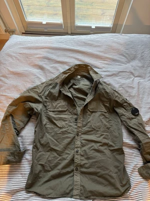 Olivgrön overshirt från C.P. Company - Snygg olivgrön overshirt från C.P. Company med klassisk krage, två bröstfickor med lock och knappar framtill. Är strl L men sitter som en M
