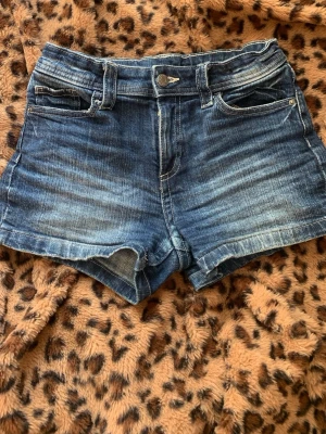 Blå denimshorts med fickor - Snygga blå denimshorts med klassisk femficksdesign och knappgylf. Shortsen har en något högre midja och slitna detaljer för en avslappnad look. Perfekta till sommaren och lätta att matcha med olika toppar.