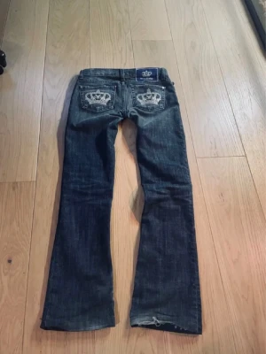 Mörkblå bootcut jeans med krona - Säljer ett par mörkblå bootcut jeans från Victoria Beckham.. Perfekta för dig som vill sticka ut lite extra! Mycket fint skick förutom att de är lite upptrampade vilket syns på första bilden. Midjemåttet är 36cm, innerbenslängden 76cm och grenmåttet 16cm.