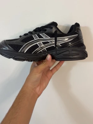  Asics gell kayon 14 - Snygga svarta sneakers från Asics med coola silvriga detaljer och meshpaneler för extra andningsförmåga. Skorna har klassisk snörning och en robust sula som ger bra grepp. Perfekta för dig som gillar sportig stil och vill ha bekväma skor till vardags.