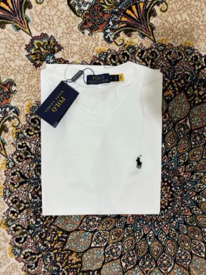 Vit t-shirt från Polo Ralph Lauren - Klassisk vit t-shirt från Polo Ralph Lauren med den ikoniska broderade loggan på bröstet. T-shirten har rund hals och korta ärmar, perfekt för en clean och stilren look. Tillverkad i mjuk bomull för maximal komfort.