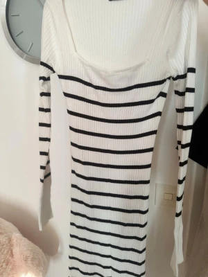 Vit ribbad långärmad klänning från Gina tricot  - Säljer en vit ribbad klänning med svarta  ränder. Klänningen har lång ärm, kroppsnära passform och är tillverkad i stretchigt material. Storlek xs 