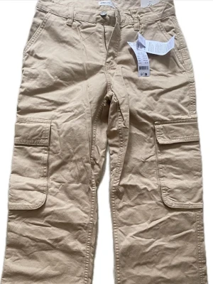 Beige cargobyxor från Gina tricot  - Snygga beige cargobyxor med låg midja från Gina tricot som inte finns säljs lägre!! Har aldrig använts och är i ny skick med prislappen på!!!