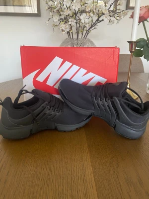 Svarta Nike Presto sneakers - Säljer ett par helsvarta Nike Presto sneakers med mesh-ovandel och plastdetaljer vid snörningen. Skorna har en sportig och clean look med rund tå och tjock sula. Perfekta för dig som gillar stilrena och bekväma sneakers från Nike.