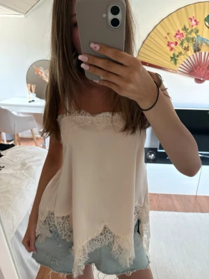 Ljusbeige spetsdetaljerad linnetopp - Säljer en ljusbeige linnetopp med tunna axelband och vackra spetsdetaljer längs både överkant och nederkant. Toppen har en flowy passform och smockad rygg för extra komfort. Perfekt för varma dagar och en söt, feminin look.