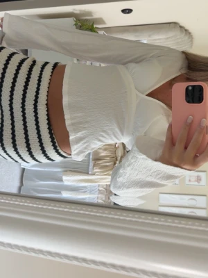 Vit omlottopp med v-ringning - Säljer en vit omlottopp med v-ringning och långa, vida ärmar. Toppen har en lätt strukturerad yta och sitter snyggt figurnära över bysten. Perfekt att styla med både jeans och kjol för en trendig look.