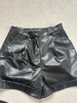 Svarta  skinnshorts från  Zara ⚡️⚡️ - Snygga svarta  shorts i skinnimitation från Zara. Har fickor fram och en dekorativ ficka bak. Perfekta för en trendig Stockholmsstil look.