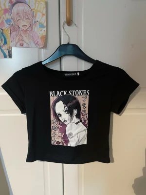 NANA Svart croppad t-shirt Black Stones - Svart croppad t-shirt från okänt märke ”MEINUODUO” med tryck av anime karaktären NANA och texten 'BLACK STONES' på bröstet. T-shirten har korta ärmar och rund hals. Materialet känns mjukt och stretchigt, troligen polyester. Storleken är S men är rätt så tajt så skulle säga XS. Säljer då den inte passar mig (OANVÄND) Köpte den utomlands, den är inte från shein/temu. Bless 🙏🏻