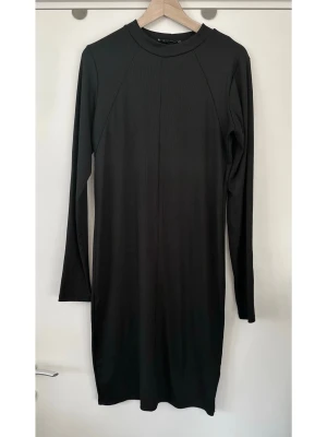 Gina Tricot - Svart långärmad klänning - XL - Svart ribbad klänning från Gina Tricot i storlek XL. Långa ärmar och rund halsringning, i stretchigt halvglansigt material. Klänningen har en figurnära passform och slutar ovanför knät. En mångsidig klänning som passar för olika tillfällen. Mycket gott skick, som ny!