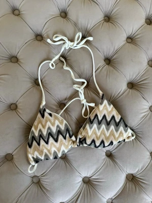 Zigzag bikiniöverdel från Becksöndergaard - Snygg bikiniöverdel från Becksöndergaard med zigzag-mönster i beige, svart och vitt. Triangelformad modell med knyt i nacken och ryggen. 