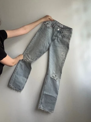 Ljusa raka jeans med slitningar - Säljer ett par ljusblå raka jeans med slitna detaljer och fransig fåll. Jeansen har hög midja, klassisk femficksmodell och är tillverkade i denim. Perfekta för en avslappnad och trendig look.