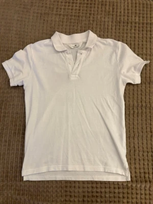 Vit piké topp - Klassisk vit piké topp med korta ärmar och krage. Toppen har knappar framtill och är tillverkad i mjukt bomullsmaterial. Perfekt till jeans eller kjol för en clean och enkel look.