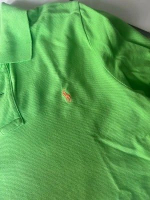 Grön pikétröja från Ralph Lauren - Snygg grön pikétröja från Ralph Lauren med klassisk krage och korta ärmar. Tröjan har den ikoniska broderade loggan på bröstet och är tillverkad i mjuk bomull som känns skön mot huden. Perfekt för en avslappnad men ändå stilren look.