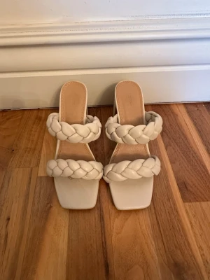 Beige flätade klackade sandaler - Säljer ett par trendiga sandaler i beige med två breda flätade remmar och fyrkantig tå. Sandalerna har en stabil blockklack och öppen häl, vilket ger en modern look. Tillverkade i konstläder med mjuk innersula för extra komfort. Endast använda en gång! OBS: FRAKTAR INOM 24H!🩷