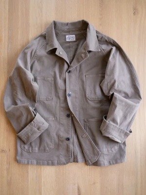 Vintage Beige Chore Jacket, size M - Stilren beige overshirt i kraftig bomull. Jackan har klassisk krage, raka ärmar och fyra stora utanpåfickor framtill. Perfekt lager-på-lager-plagg med avslappnad passform och snygga detaljer som synliga sömmar och knäppning framtill.
