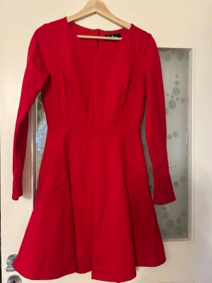 Röd långärmad klänning från Vero Moda - Snygg röd klänning från Vero Moda med lång ärm och rund halsringning. Klänningen har en utställd kjol och dragkedja i ryggen för enkel påklädning. Perfekt för dig som vill sticka ut med en klassisk och stilren look.