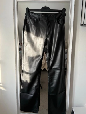 Svarta skinnbyxor från BikBok - Snygga svarta skinnbyxor från BikBok med raka ben och klassisk femficksdesign. Byxorna har bälteshällor och stängs med knapp och dragkedja. Perfekta för en trendig look och lätta att matcha med olika outfits.