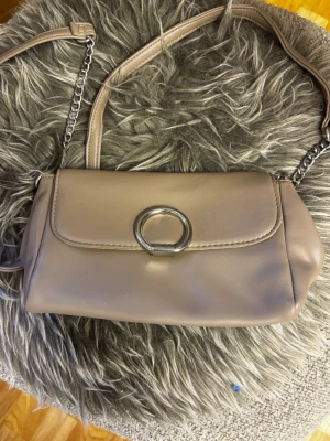 Beige axelremsväska med silverdetalj - Snygg beige handväska i slätt konstläder med axelrem som kombinerar kedja och läder från Glitter!