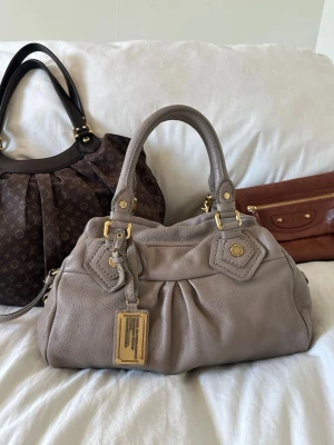 Beige Q Classic Baby Groove väska! - Så fin beige handväska i äkta läder från Marc by Marc Jacobs. Den ikoniska modellen Q Classic Baby Groove! En populär och eftertraktad vintagemodell med gulddetaljer och dubbla handtag. Långa bandet medföljer ej. Så snygg vintageväska i toppskick, inga skavanker. Ren invändigt och fina gulddetaljer. Svår att få tag på i detta skick. Skriv privat för fler bilder 🤍  Mått: Lilla modellen. 34x18x12 cm (undersida)  Kan hämtas hemma hos mig i Nacka eller skickas 🤍 