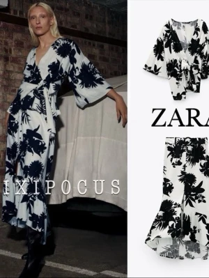 SET med blus och kjol från Zara - Set med omlottblus och kjol med skärp från Zara med svart blommigt mönster på vit bakgrund. Blusen har vida ärmar, knytband i midjan och asymmetrisk nederkant. Kjolen har dekorativa knappar fram och slits.  blus strl M, kjol strl S 