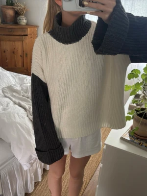 Vit och svart stickad polotröja - Säljer en oversized stickad tröja med bred polokrage. Tröjan är vit med svarta kontrastärmar och svart krage. Den har en boxy passform och långa, vida ärmar. Perfekt för lager på lager och chill stil.