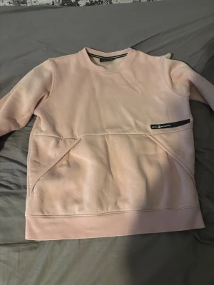 Ljusrosa sweatshirt från Sail Racing - Storlek 160 Ljusrosa sweatshirt från Sail Racing med rund hals och snygga detaljer som en svart logotyp på bröstet. Tröjan har en modern passform och är tillverkad i mjukt material med fleece på insidan. Perfekt för dig som gillar stilrena och sportiga plagg.