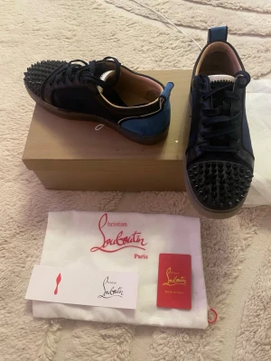Christian Louboutin svarta sneakers - Snygga svarta sneakers från Christian Louboutin med svarta nitar på tån, blå mockadetaljer. En nita från skon har lossnat som ni ser på sista bilden 🙌🏼 dom har defekter men inget man tänker på vid andvändning om du har några frågor tveka inte att höra av dig mvh olle