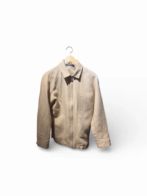 Beige tunn J.Lindeberg jacka med dragkedja - Säljer en stilren beige jacka i tunnare material med klassisk krage och dragkedja framtill. Jackan har raka ärmar och enkel design. 